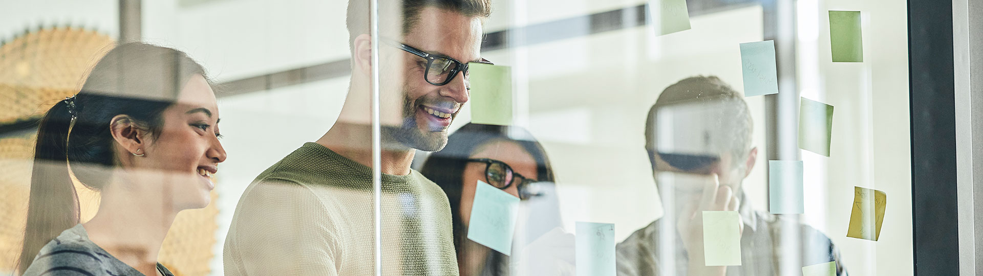 Gruppe von Menschen schaut auf eine Glaswand mit PostIt